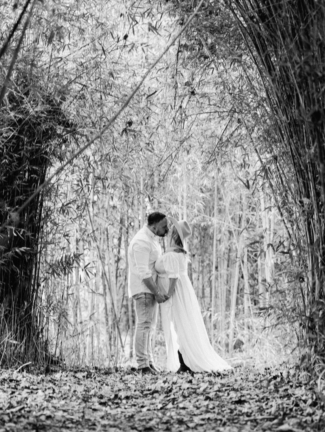 Black and white photo of a couple kissing under a bamboo arch surrounded by lush forest foliage.