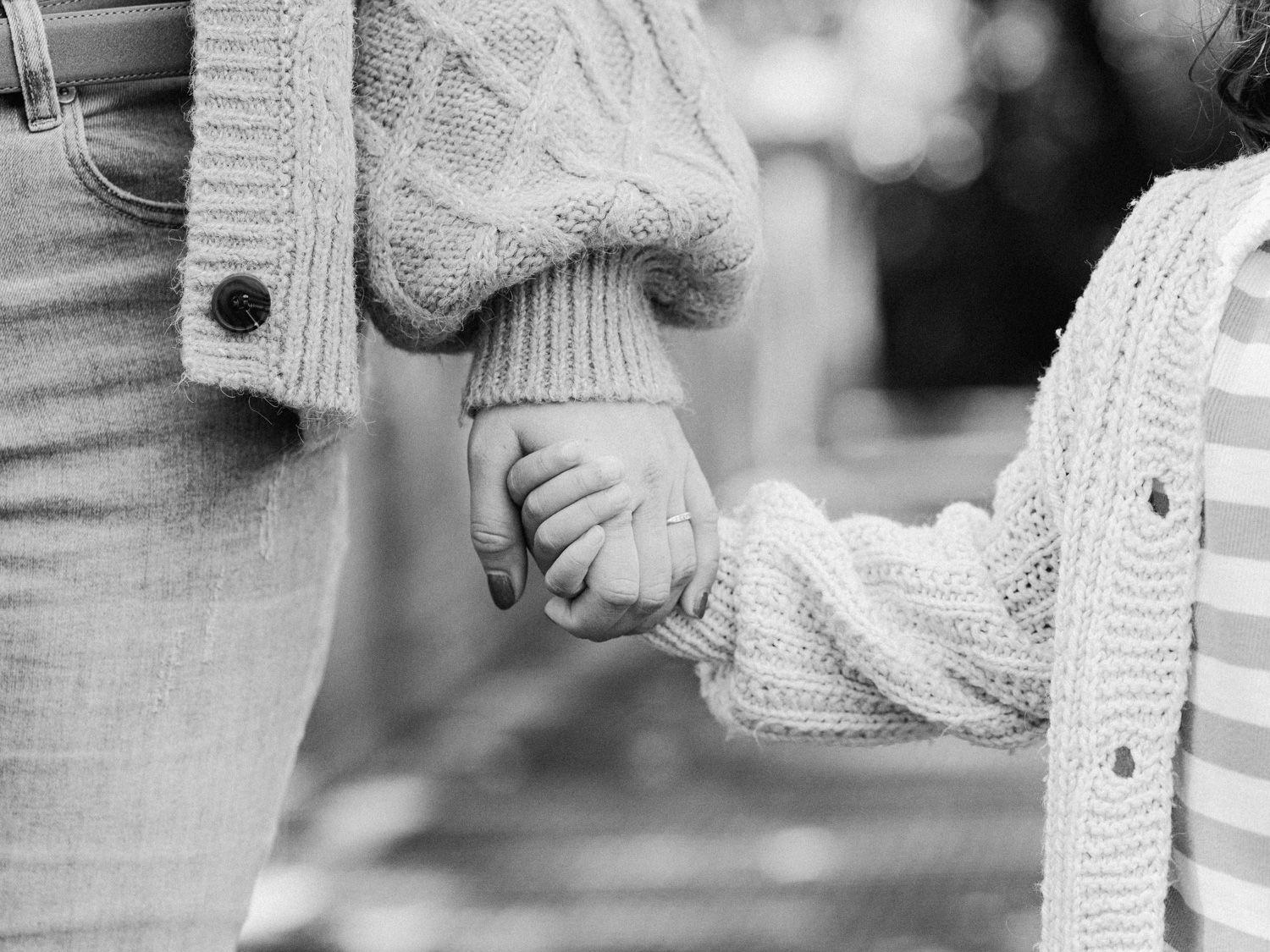 Black and white photo of a parent and child holding hands, both wearing cozy knit sweaters outdoors.
