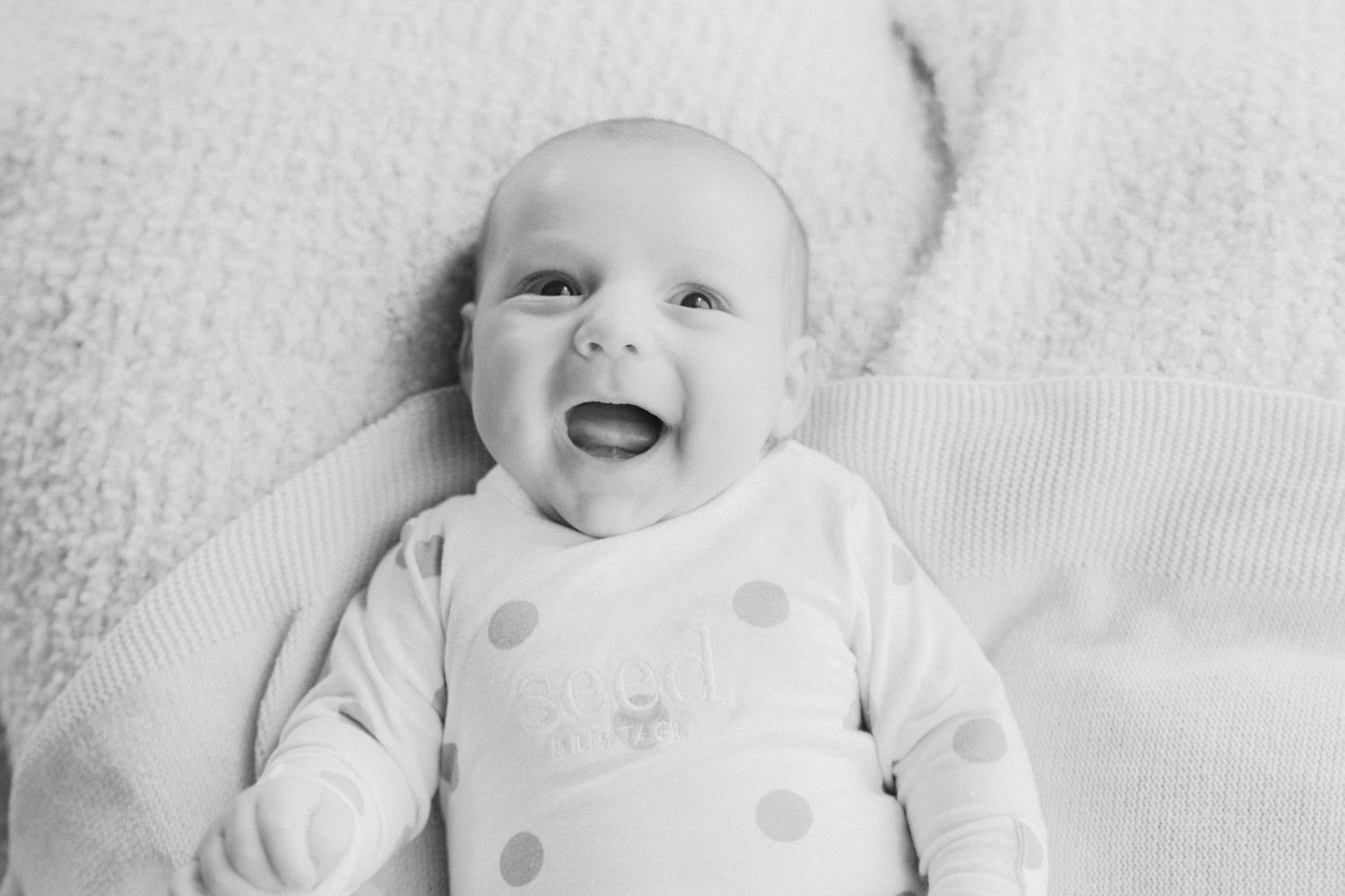 Adorable smiling baby in polka dot onesie lying on soft blanket, black and white newborn portrait photography.