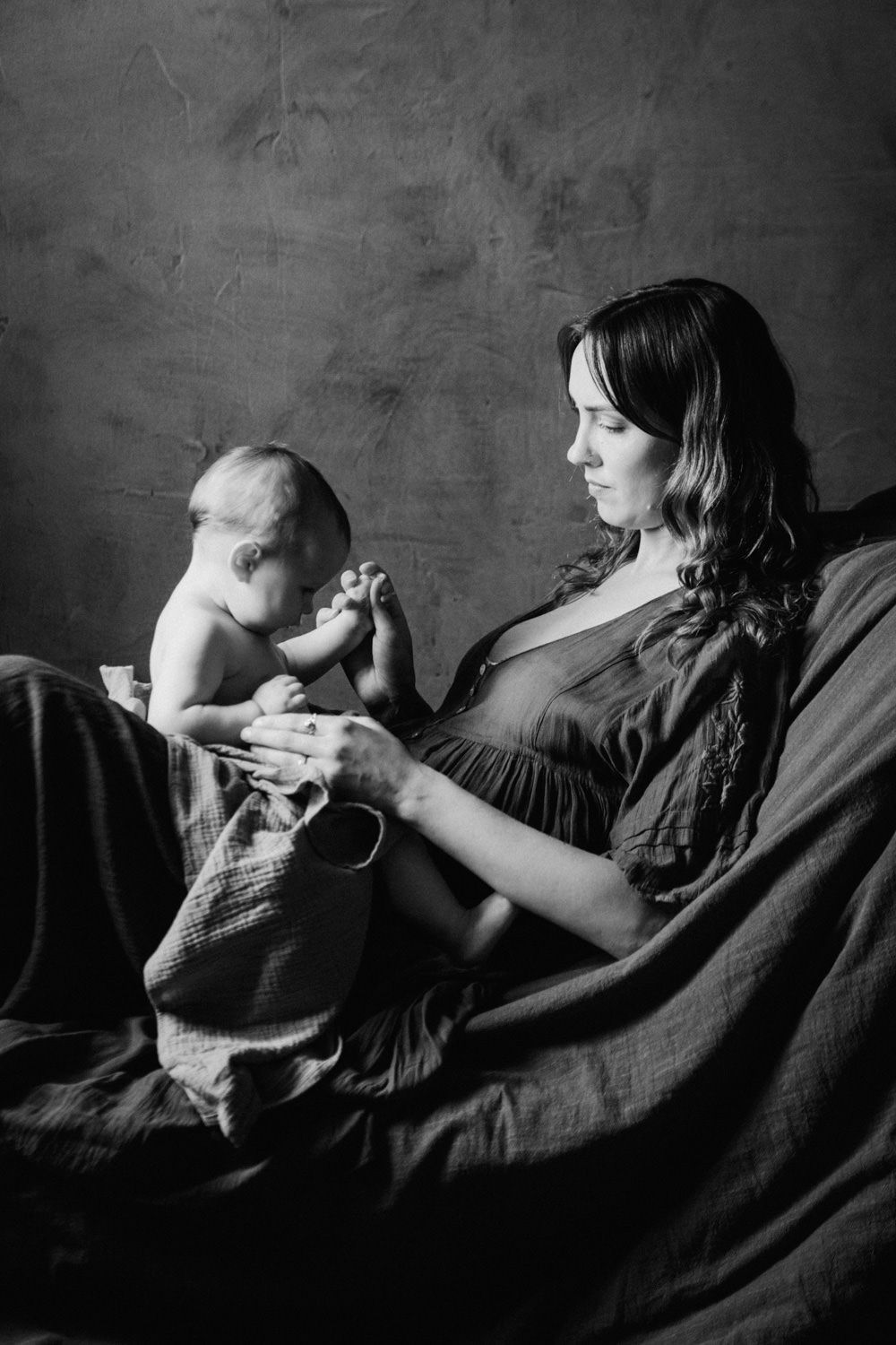 Black and white photo of a mother tenderly holding her newborn baby's feet while reclining on a bed.