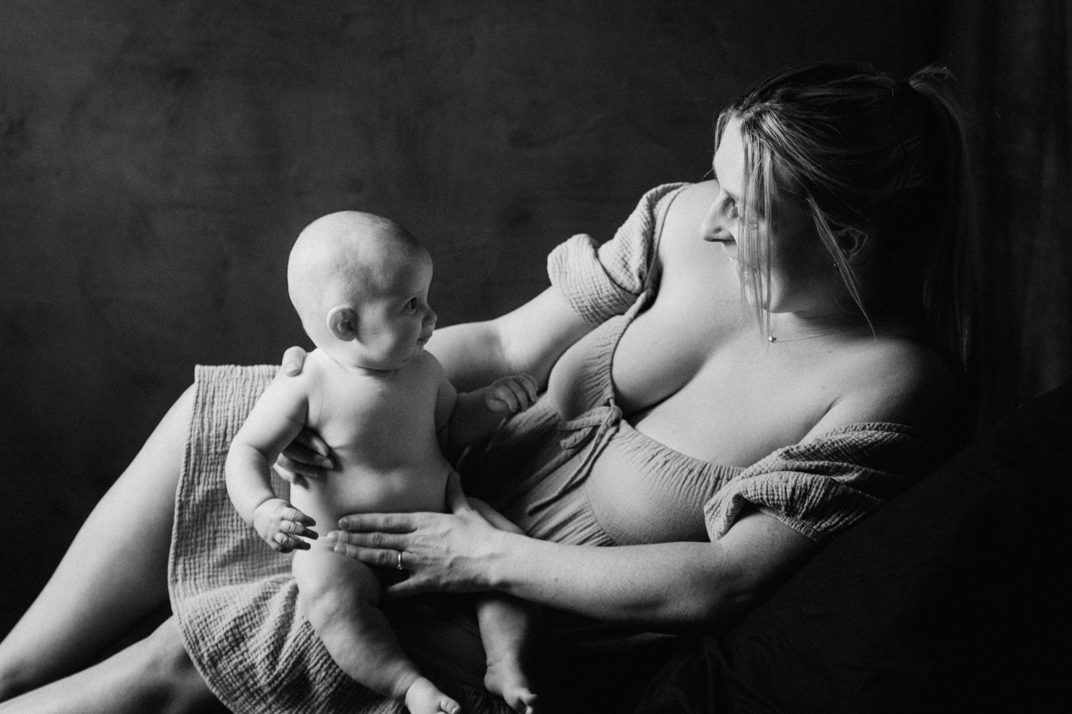 Black and white photo of a mother tenderly holding her baby on her lap in a studio portrait session.