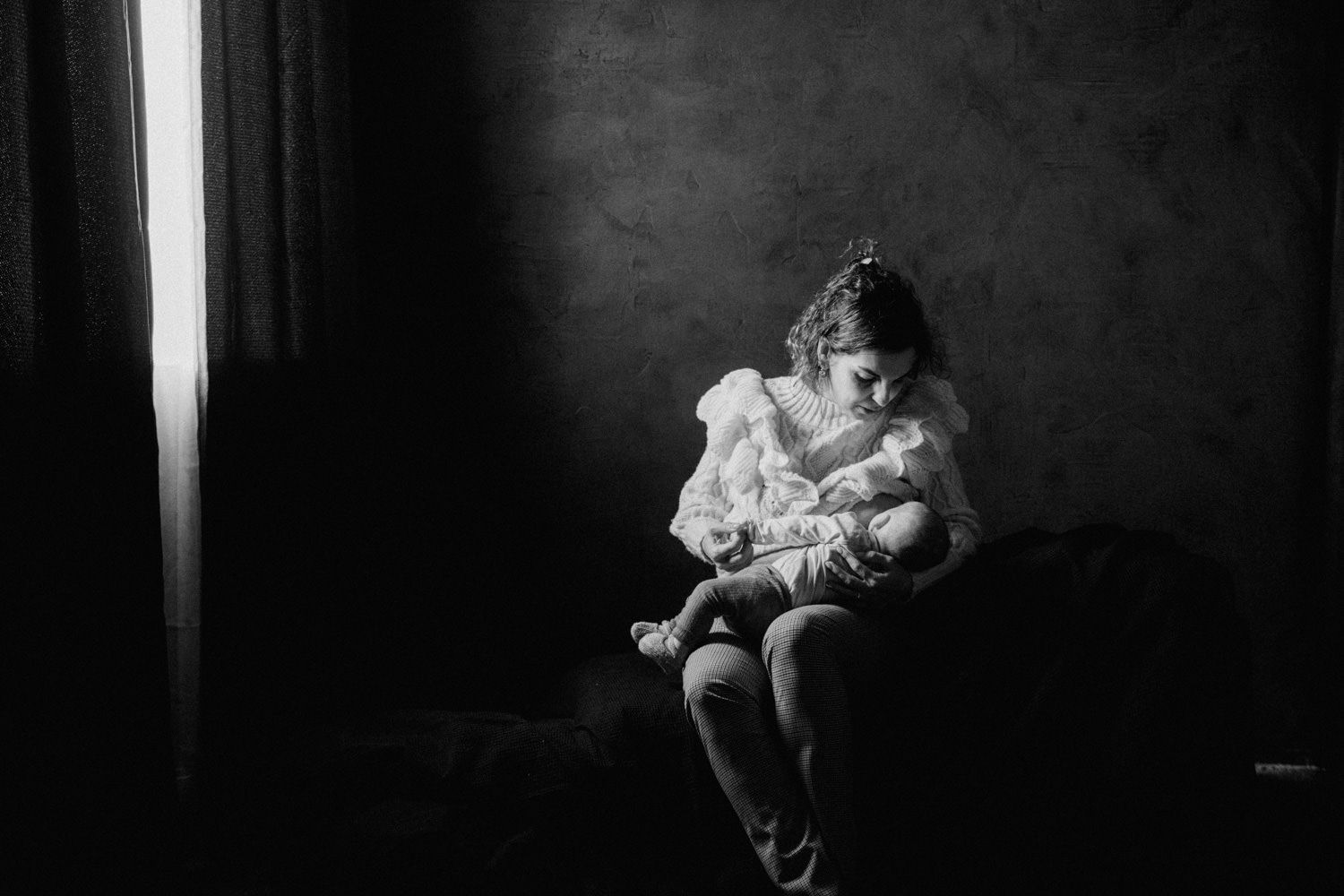 Black and white photo of a mother tenderly holding her newborn baby in a dimly lit room.