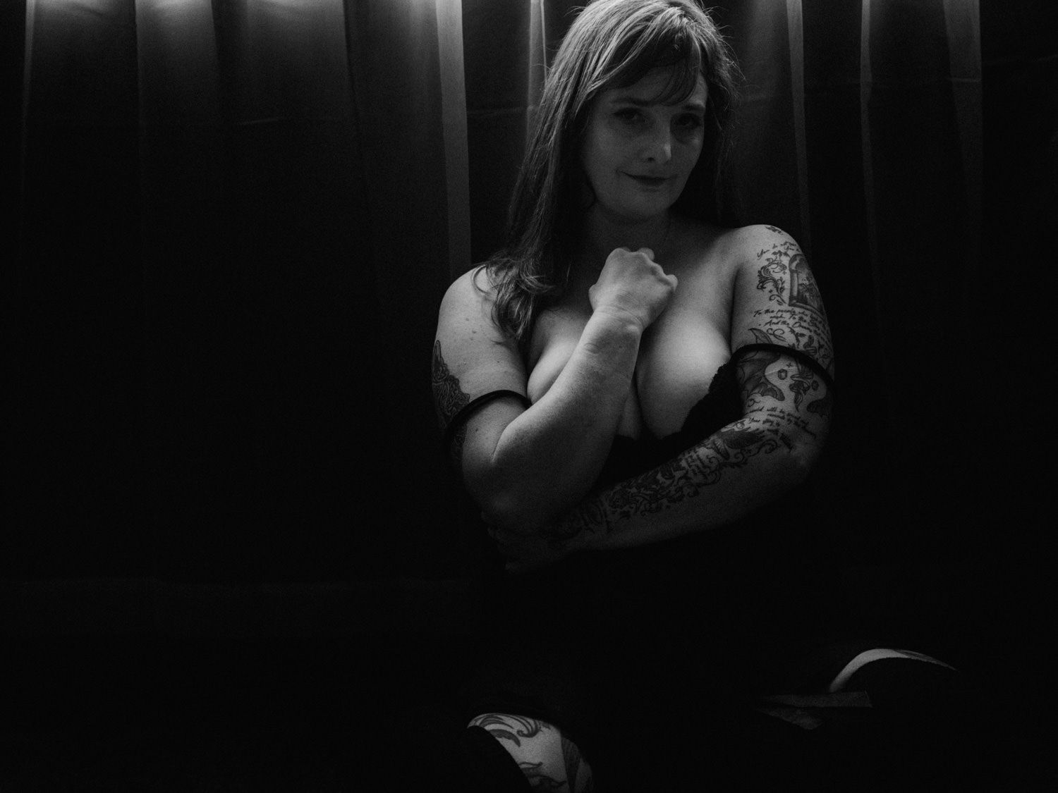 Black and white portrait of a woman with tattoos posing in dramatic low-key lighting.