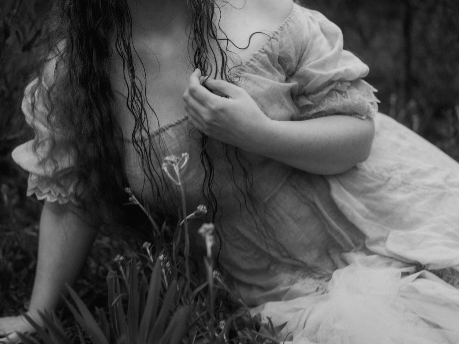 Black and white photo of a woman in a vintage dress sitting among flowers in a garden.
