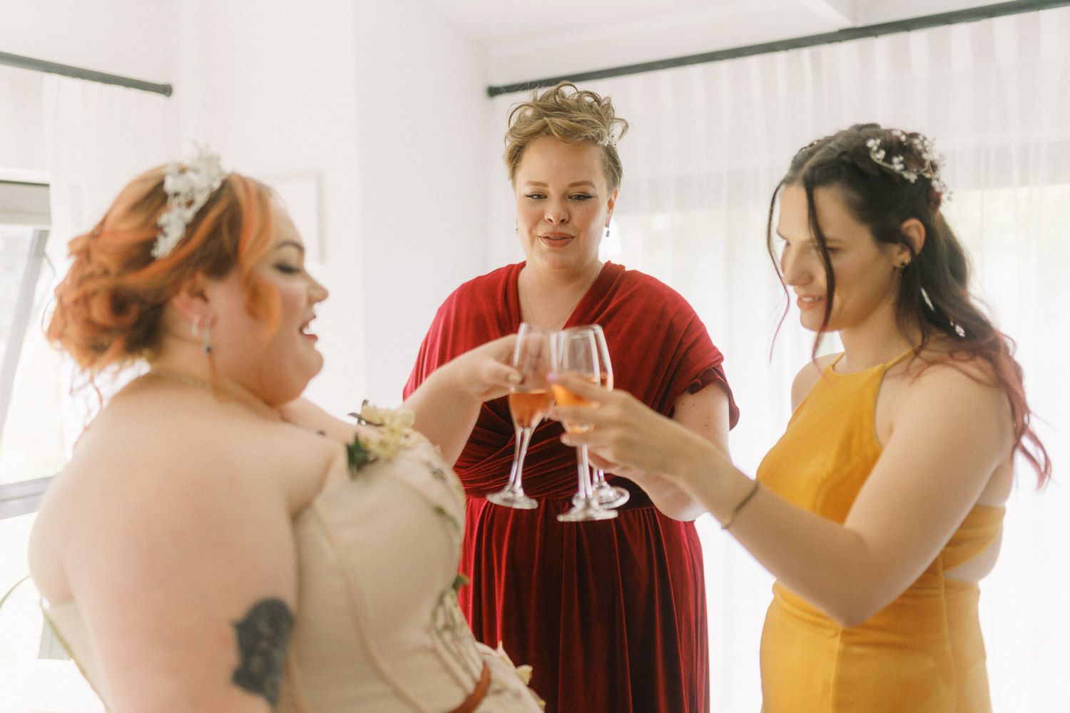Bride and bridesmaids in colorful dresses toasting with champagne glasses during wedding preparations.