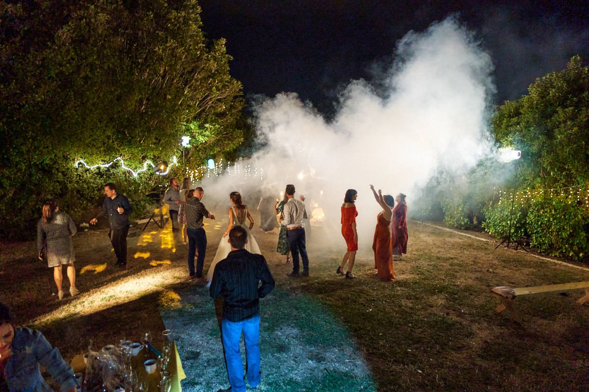 People gathered outdoors at night surrounded by dramatic white smoke during a festive evening celebration.