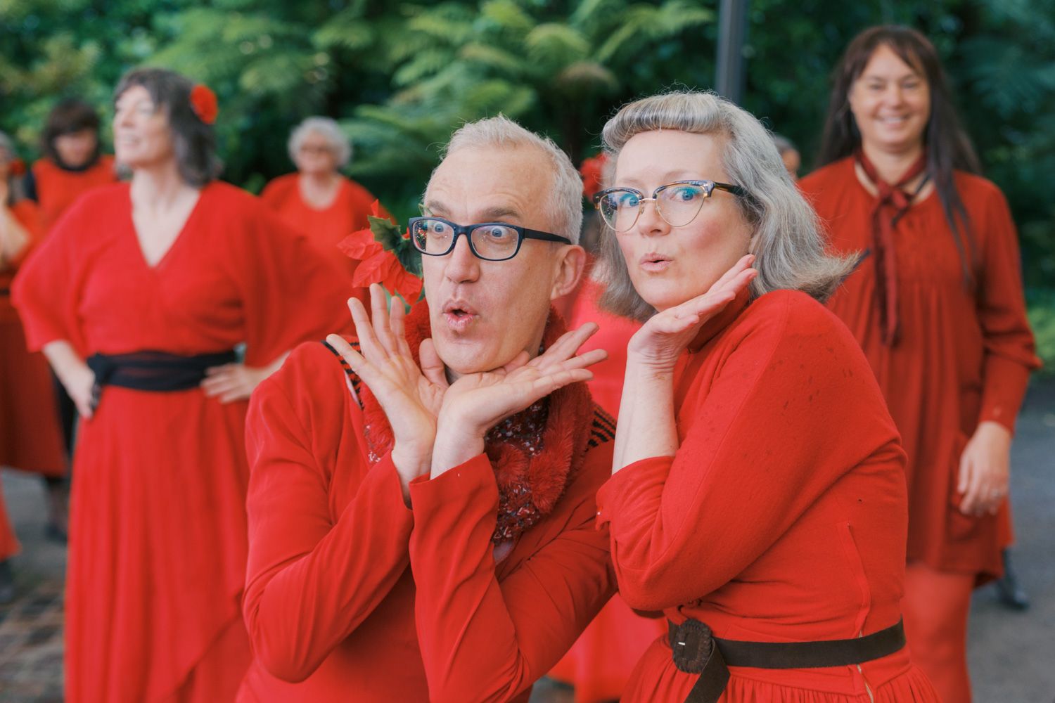 Group of adults in matching red dresses posing playfully outdoors, blowing kisses at the camera.