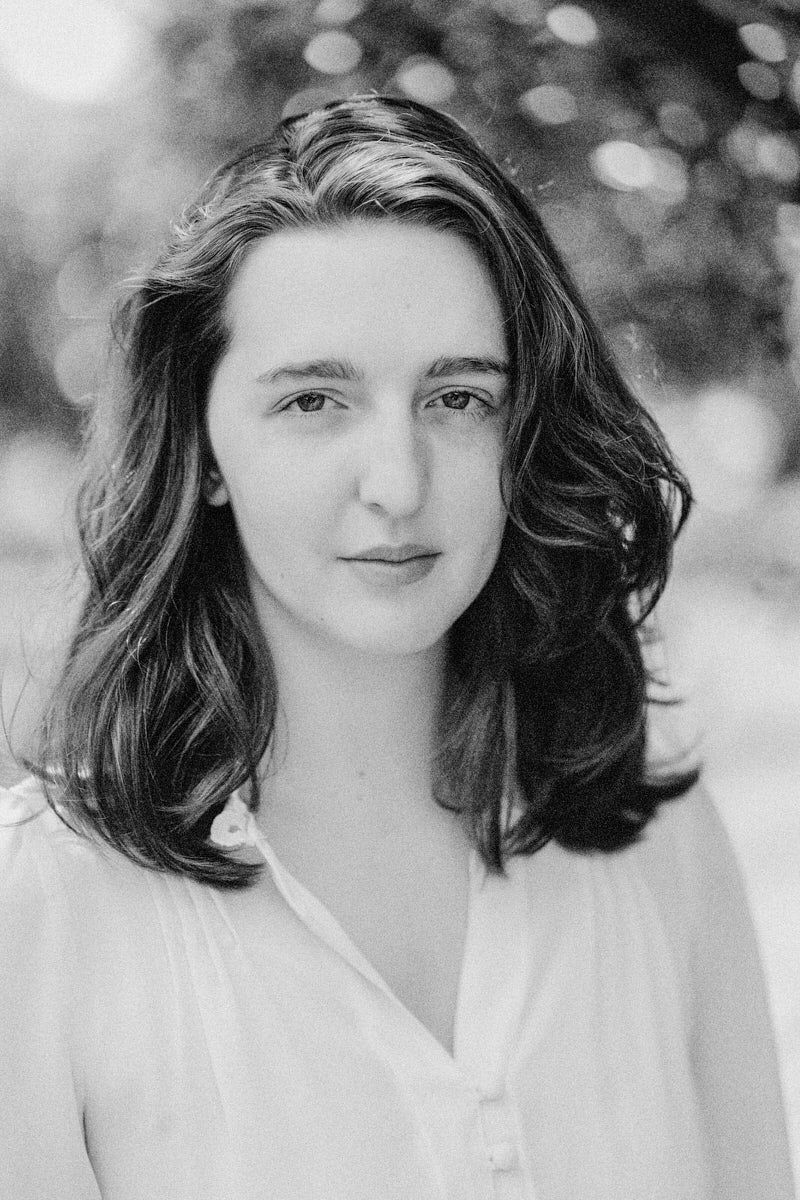 Black and white portrait of a young woman with shoulder-length dark hair wearing a white blouse outdoors.