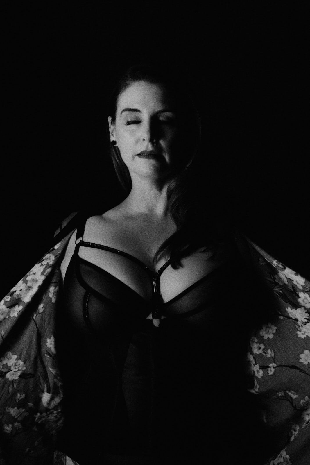 Black and white boudoir portrait of a woman in lingerie with floral robe against dark background.