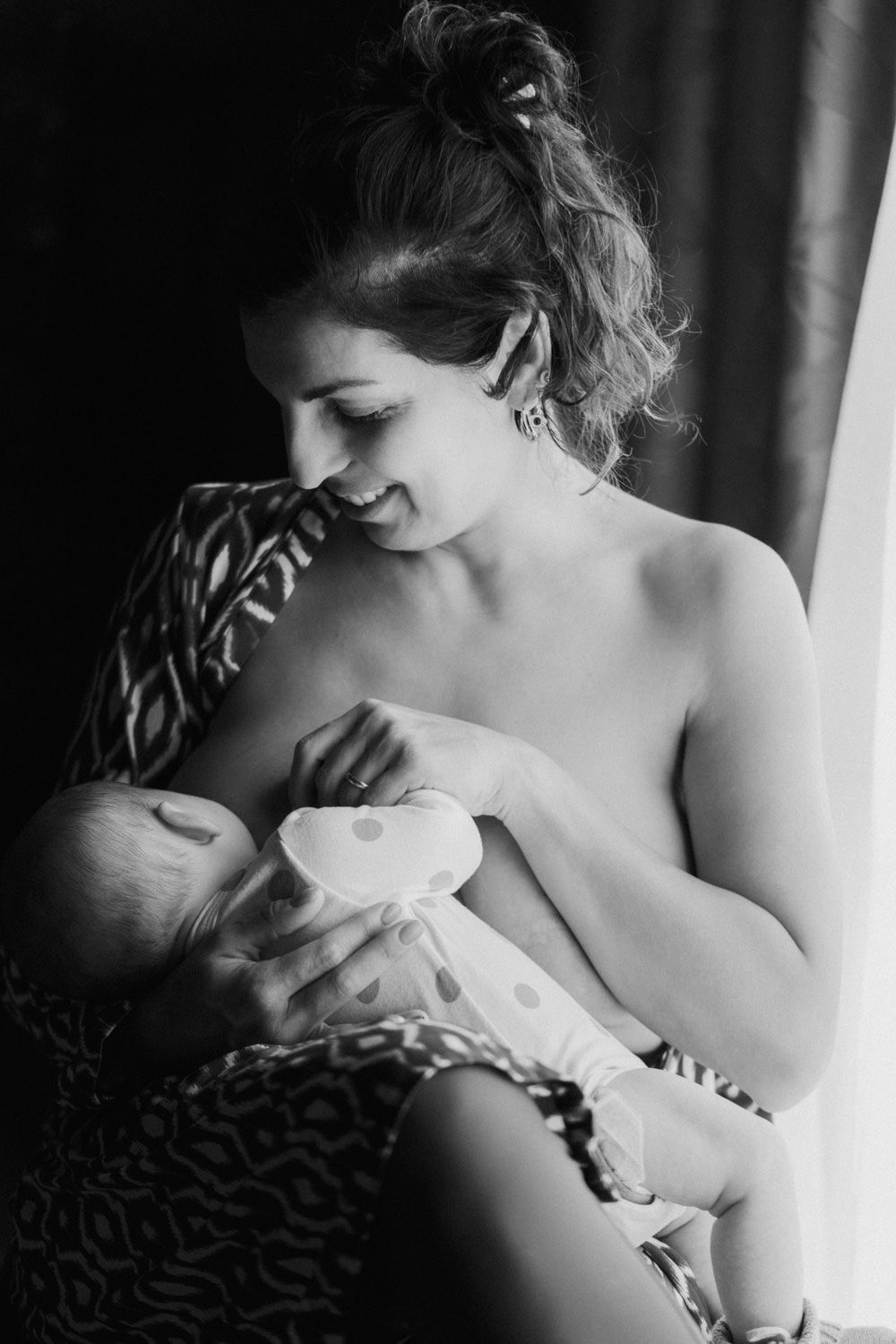 Black and white photo of a mother breastfeeding her newborn baby while sitting in a patterned chair.