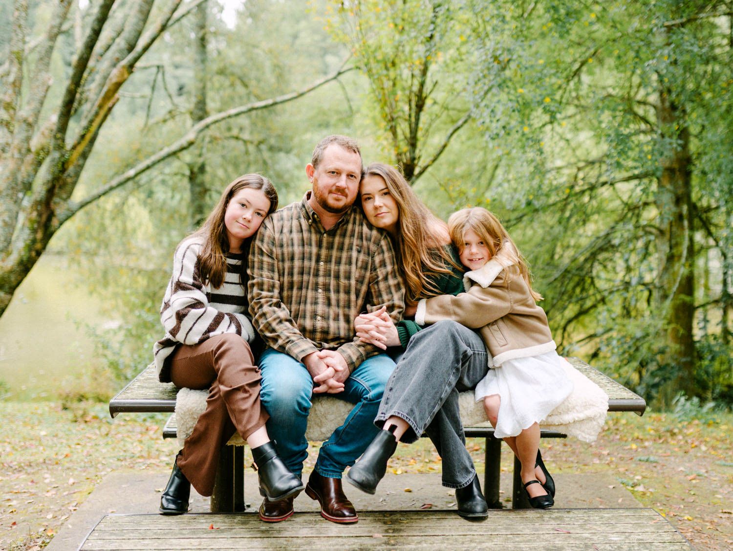 Family of four posing on a park bench surrounded by lush green trees in a forested outdoor setting.