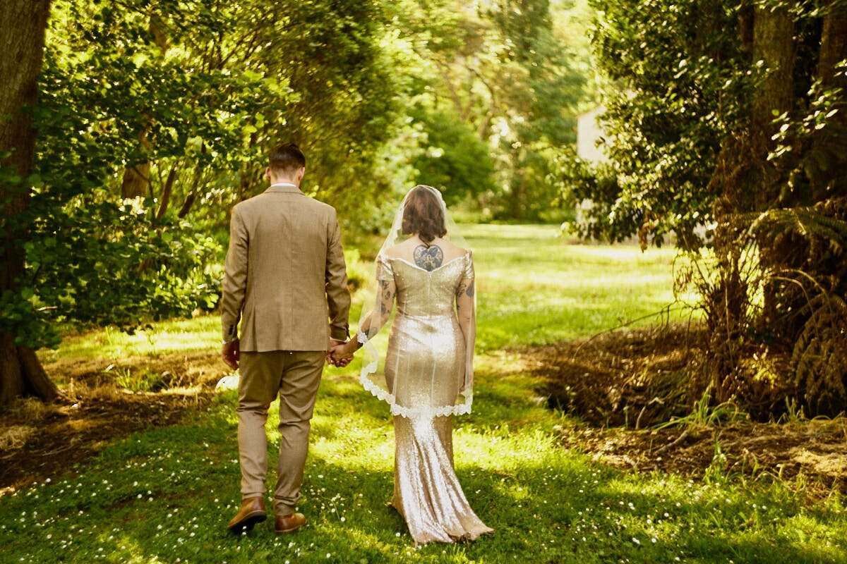 Bride and groom walking hand in hand through a lush green garden path on their wedding day.