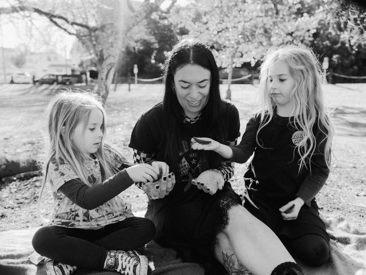 Black and white photo of a woman and two blonde girls sitting outdoors in a park.