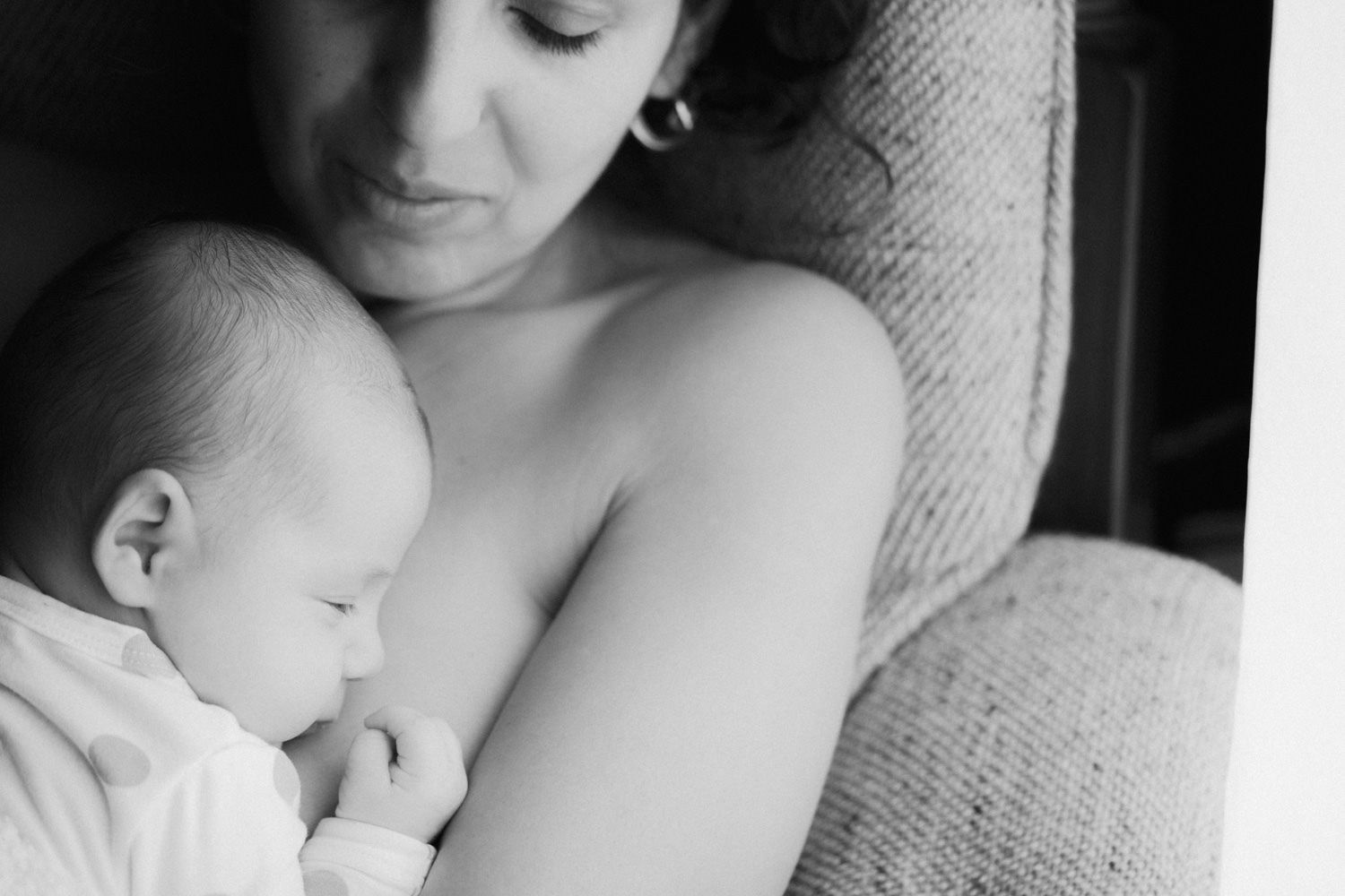 Black and white photo of a mother tenderly breastfeeding her newborn baby while seated in a cozy chair.
