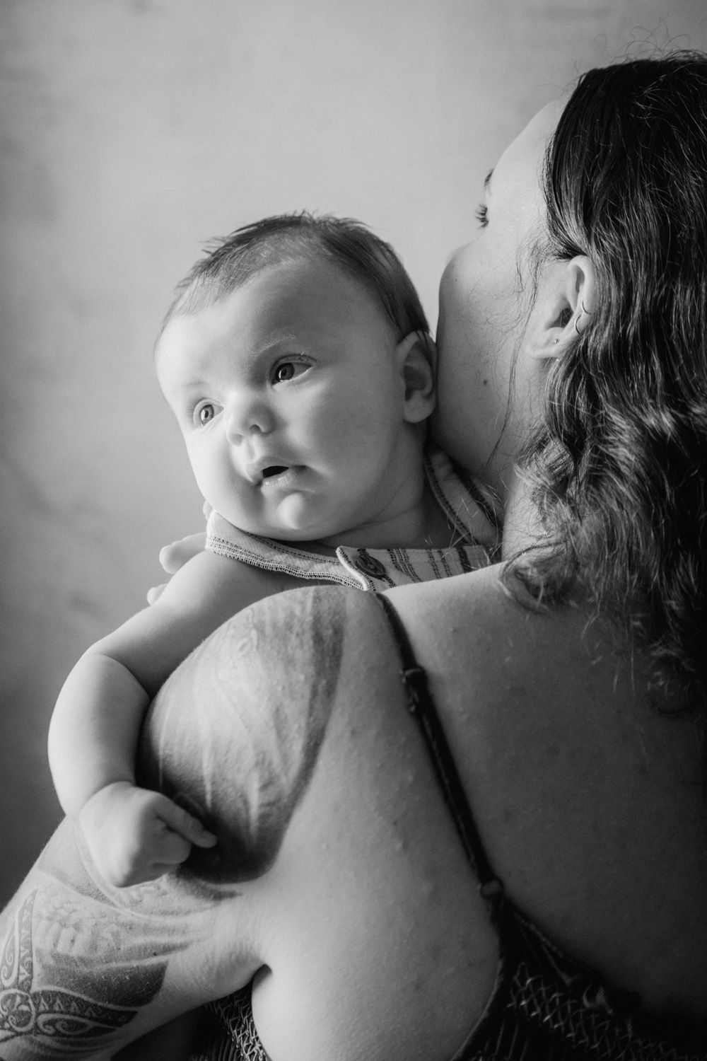 Black and white photo of a mother tenderly kissing her infant baby while holding them close.