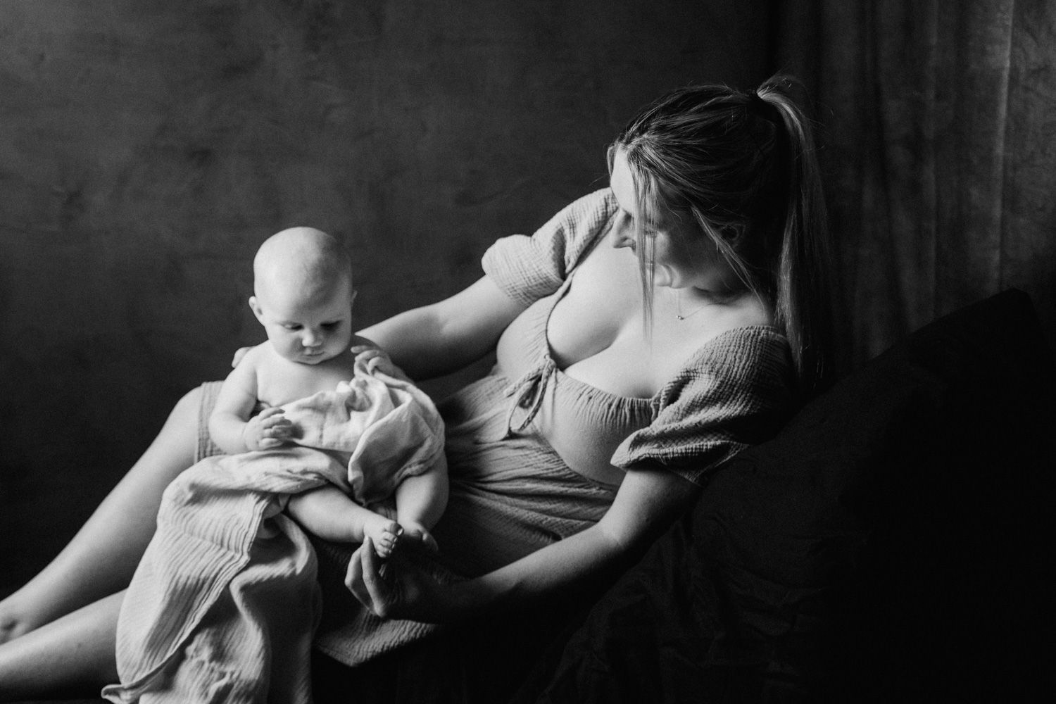 Black and white photo of a mother tenderly breastfeeding her baby while seated in a chair.