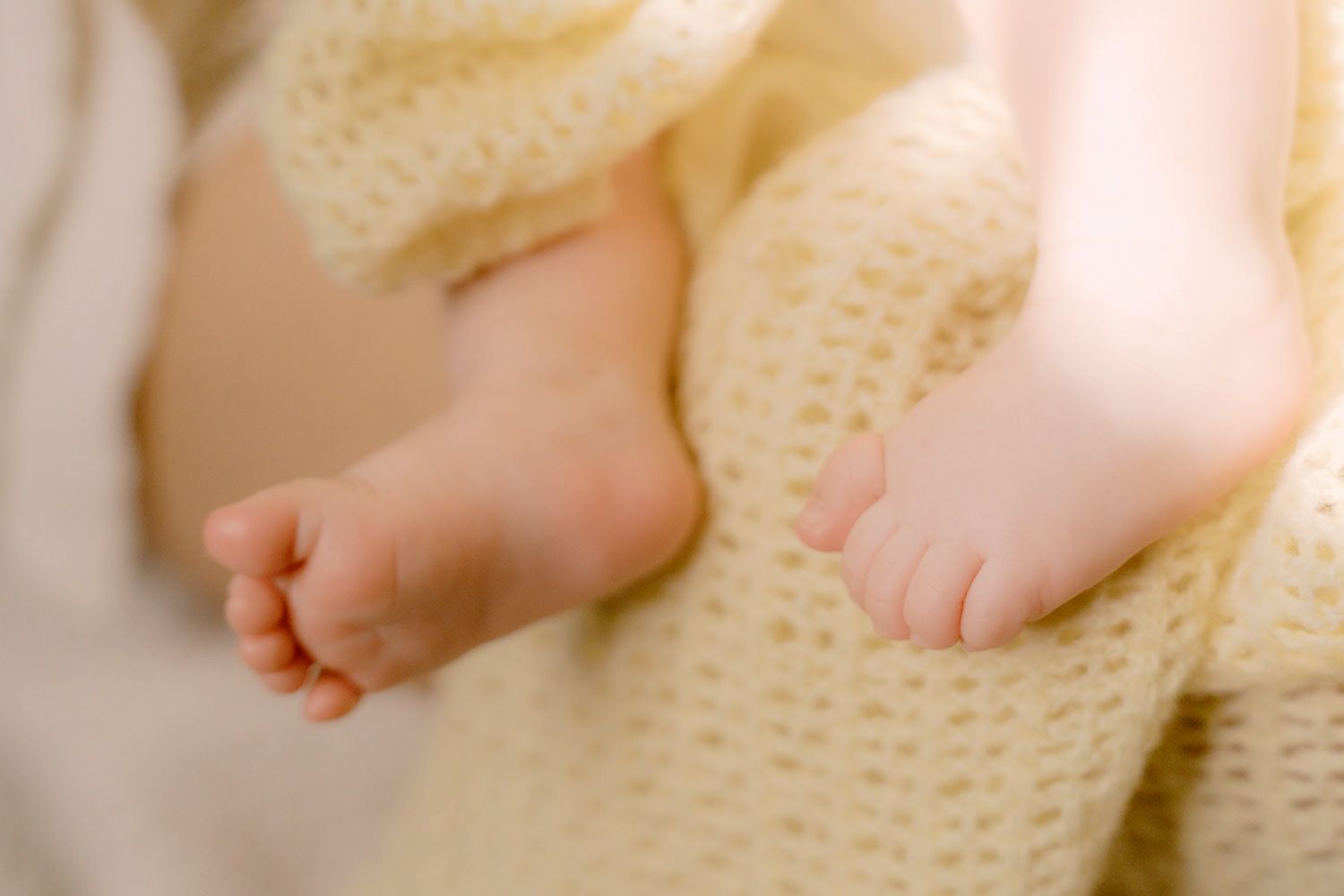 Close-up of tiny newborn baby feet wrapped in a soft yellow knit blanket.