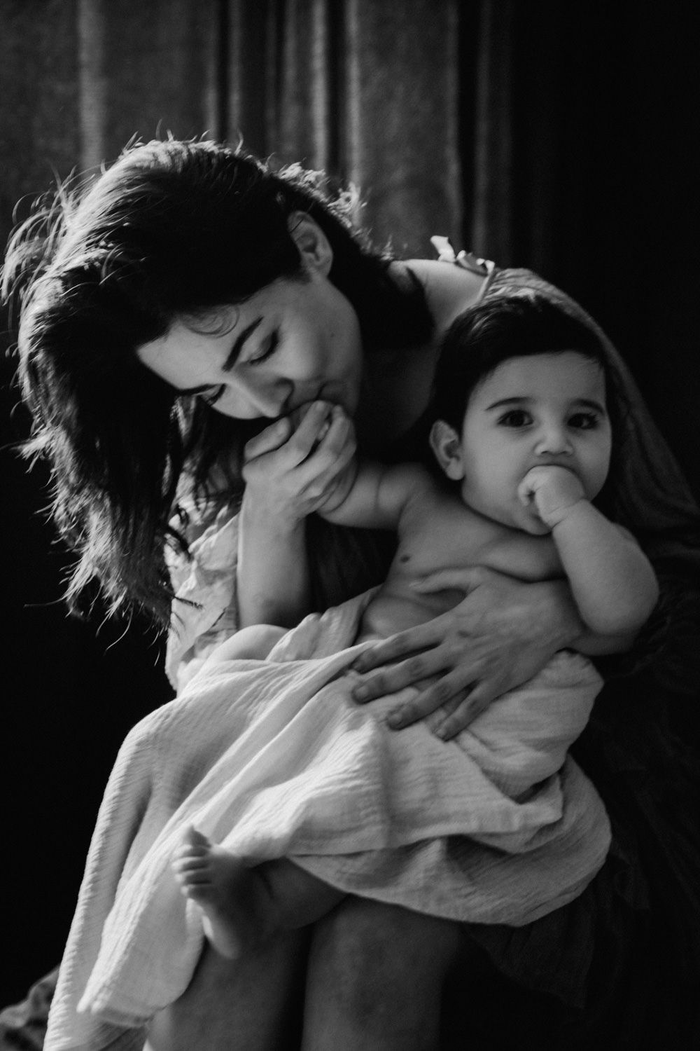 Black and white photo of a mother tenderly holding her baby wrapped in a soft blanket.