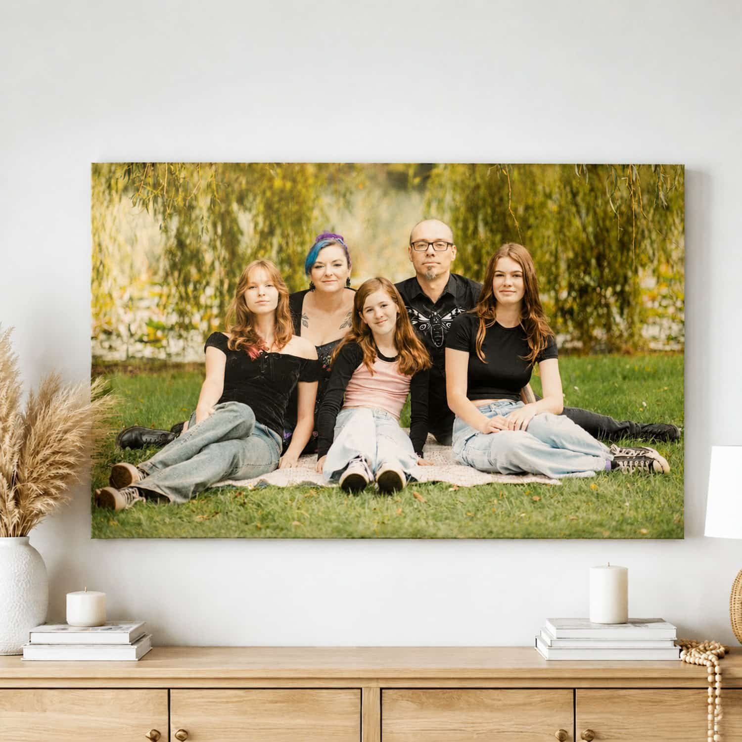 Family of five posing outdoors on grass with autumn trees, displayed as a canvas print on a living room wall.