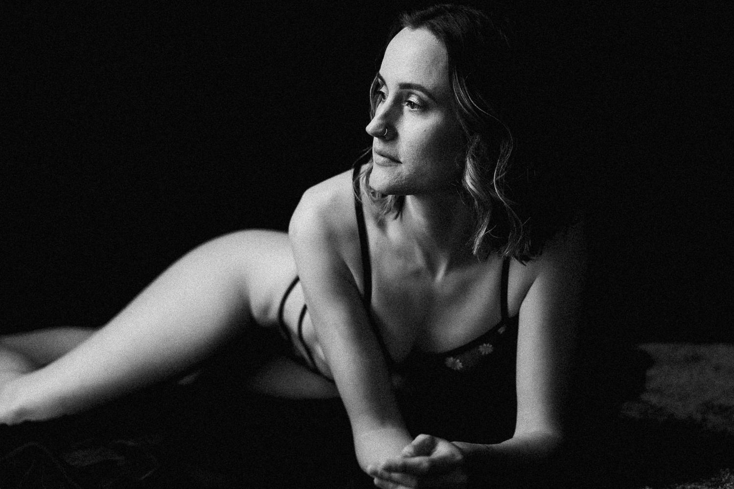 Black and white boudoir photo of a woman in lingerie posing gracefully on a dark background.
