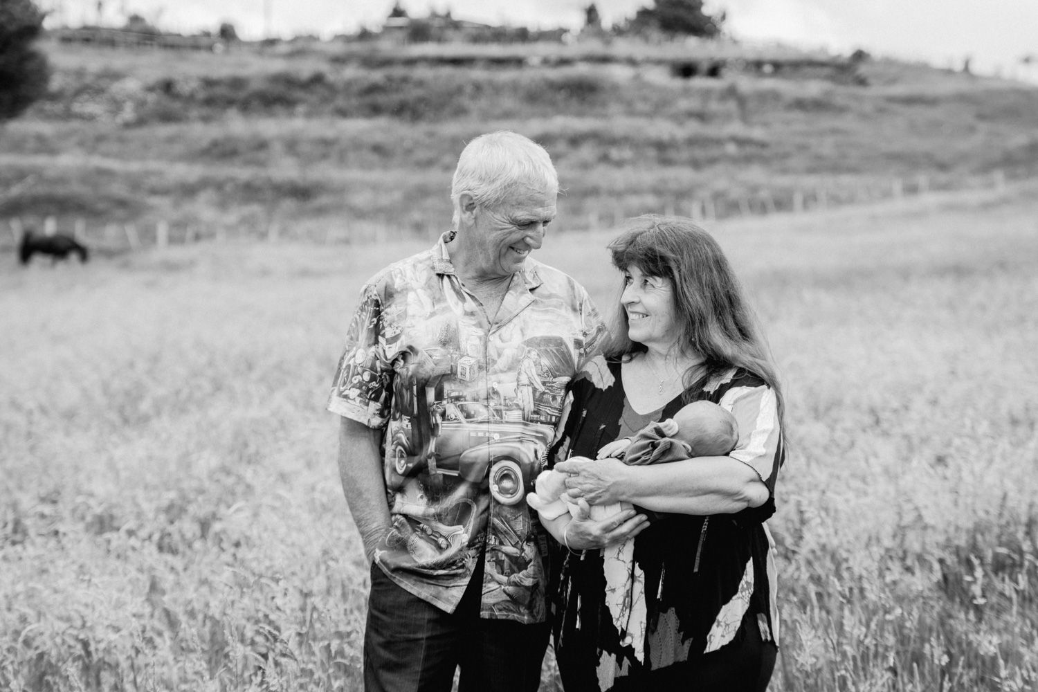 Black and white photo of a couple standing in a field holding a newborn baby.