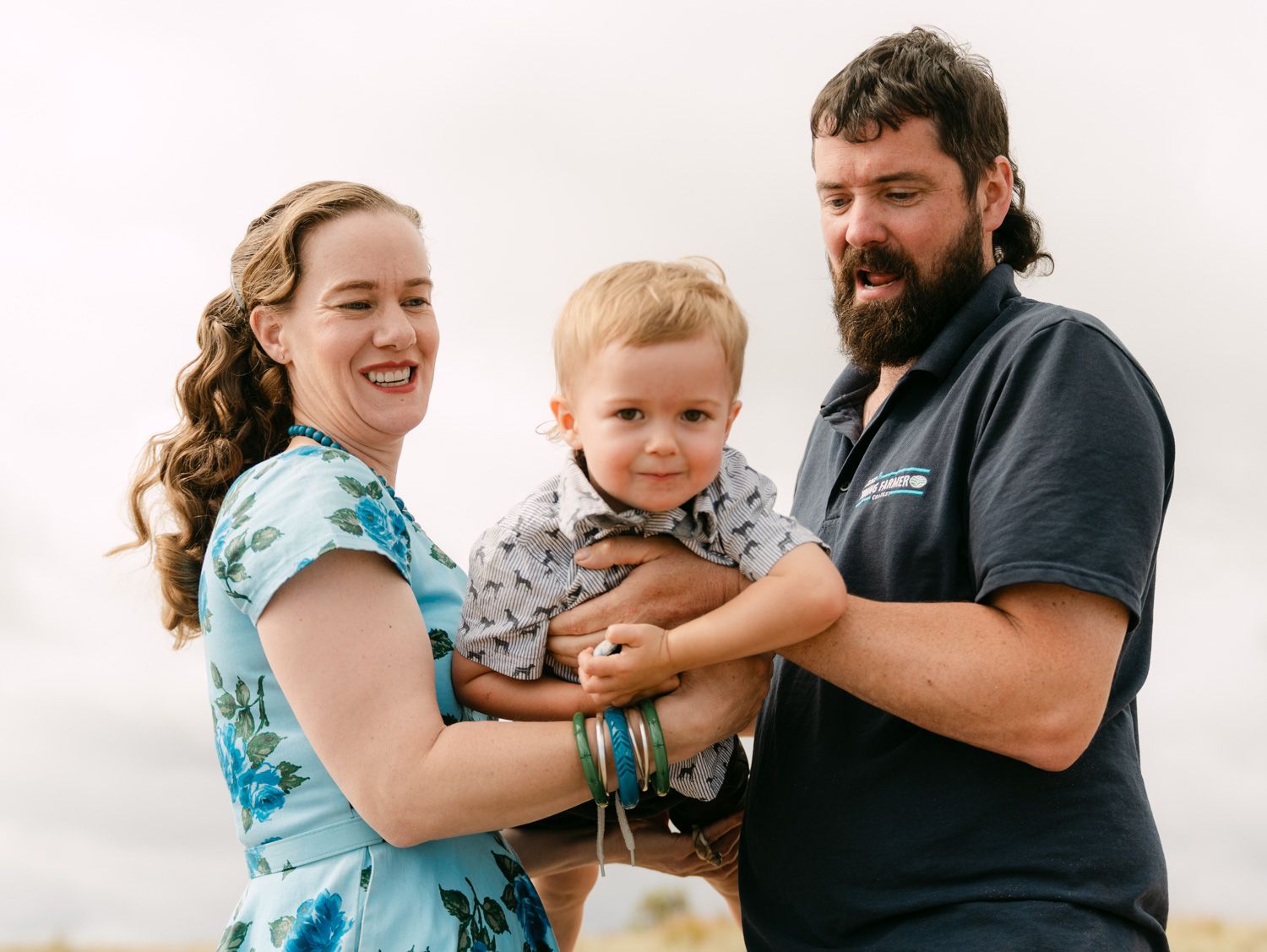 Happy family portrait of parents holding their smiling toddler outdoors on a cloudy day.
