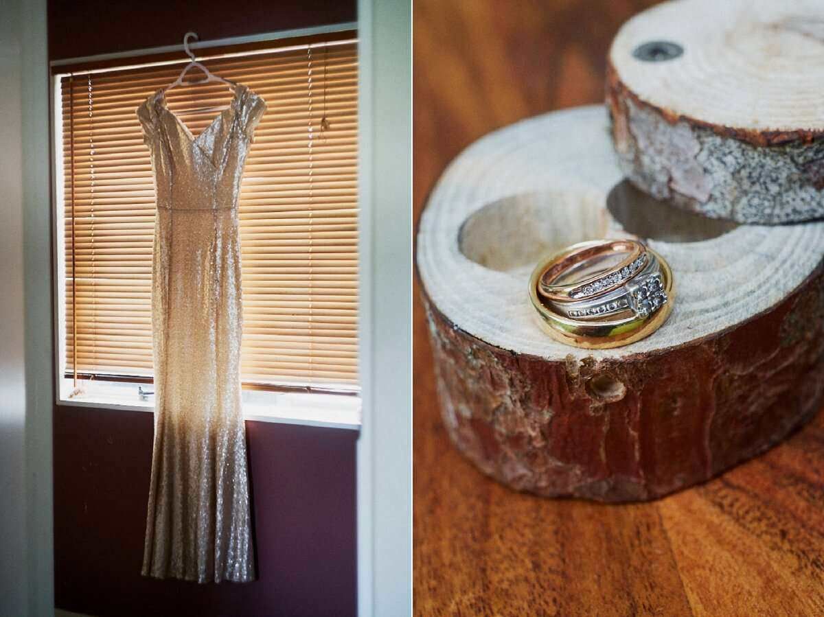 Elegant gold sequin bridesmaid dress hanging by window beside wedding rings on rustic wood slice.