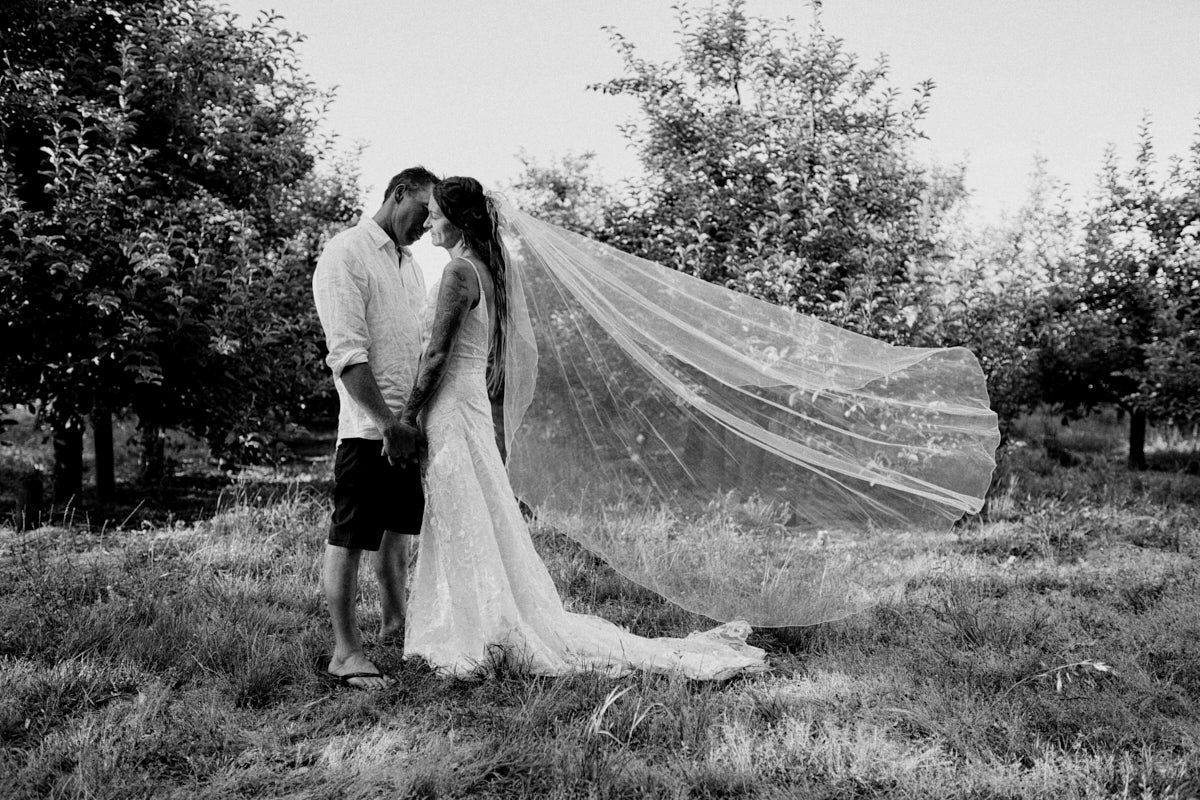 Black and white photo of a bride and groom kissing outdoors, with the veil dramatically billowing in the wind.