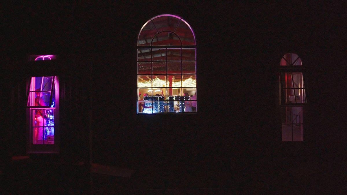 Nighttime view of illuminated arched windows glowing pink and orange from inside a dark building exterior.
