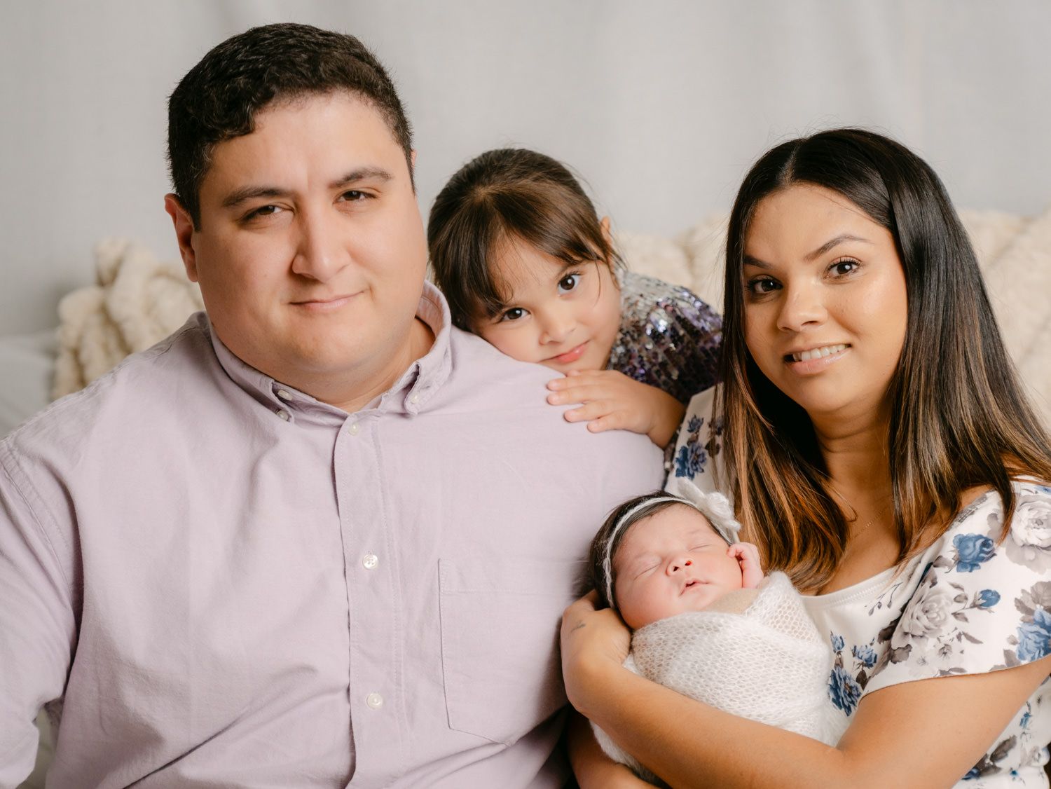 Happy family portrait with parents and two children, including a newborn baby, posing together in a bright studio.