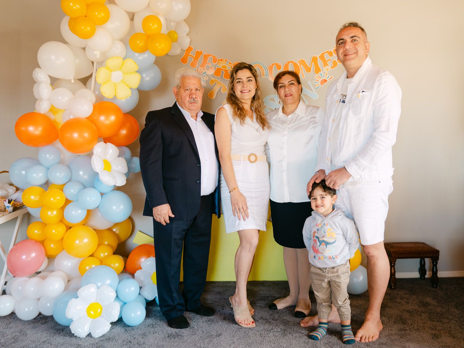 Family of five posing together at a festive party with colorful balloon arch and daisy decorations.