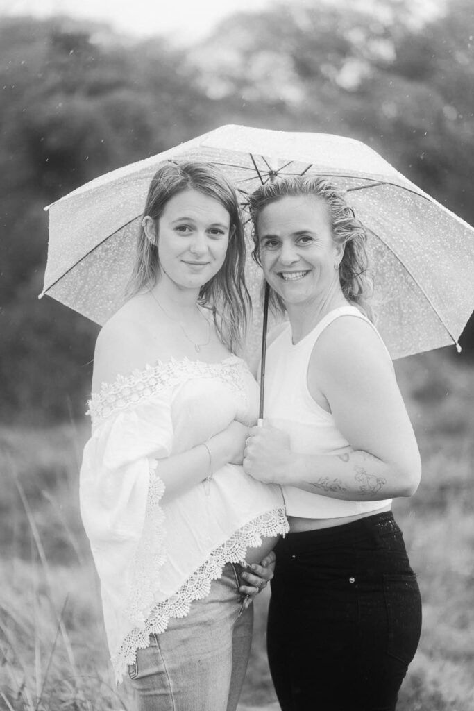Two women sharing an umbrella outdoors in a black and white portrait photo.