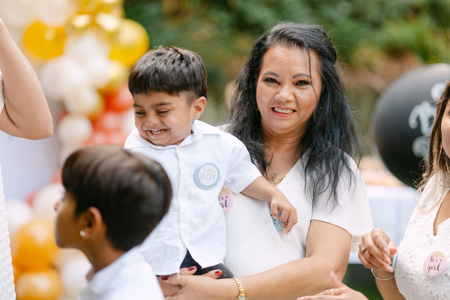 Woman smiling with young boy at colorful outdoor birthday party with balloons in background.