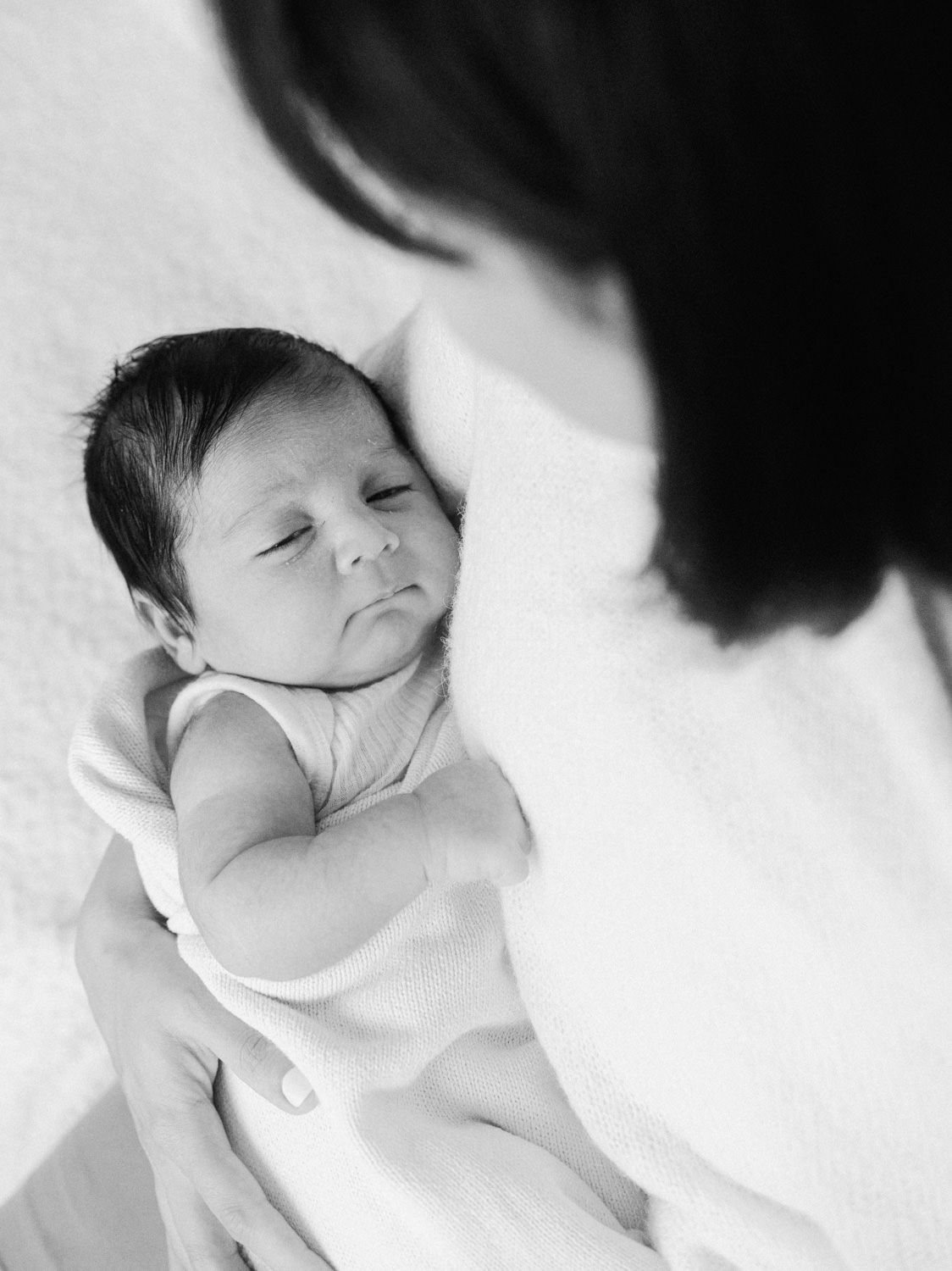 Black and white overhead view of a calm newborn baby being held by mother.