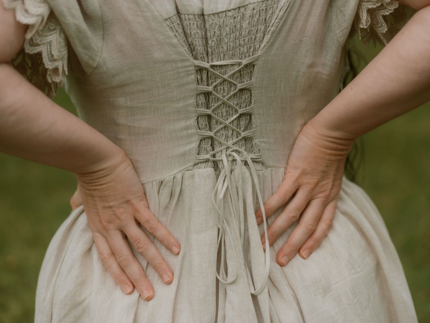 Close-up back view of cream linen corset dress with lace-up detail.