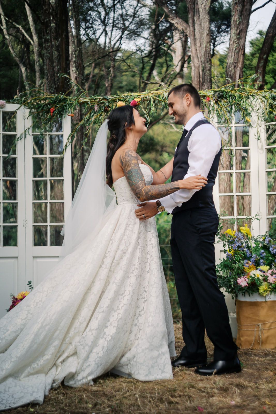 Bride and groom share a romantic moment under a floral arch at an outdoor wedding ceremony.
