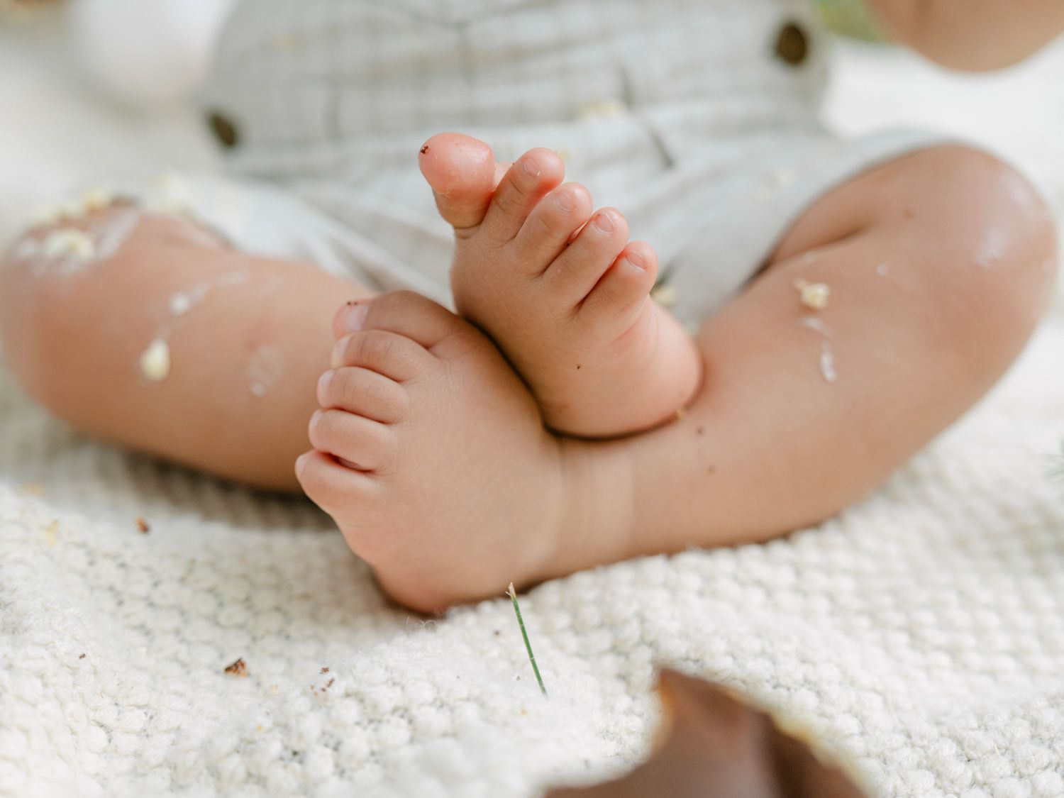 Close-up of adorable baby feet and toes resting on a soft white blanket with small flower petals scattered around.