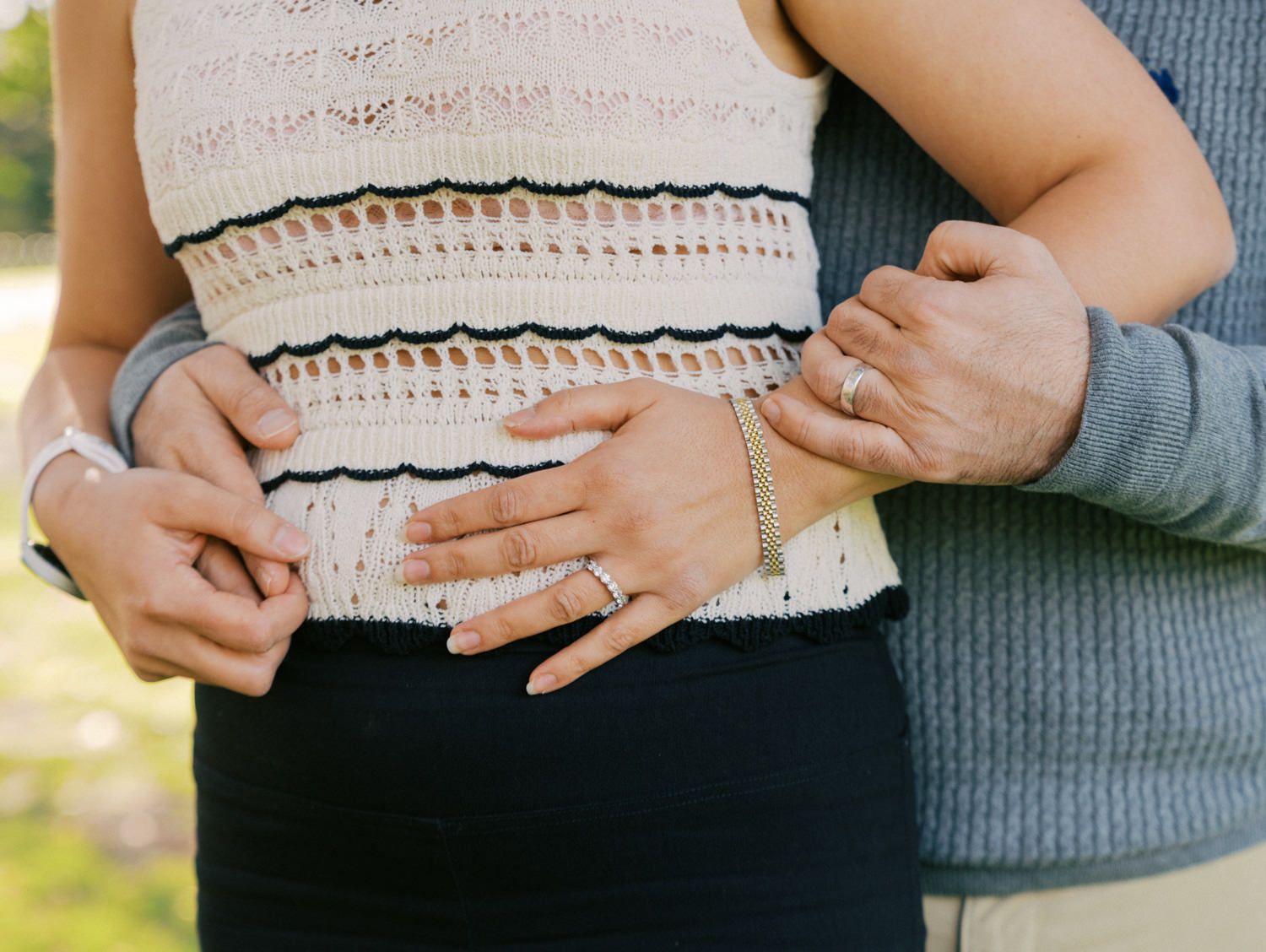 Couple embracing, showing engagement ring and bracelet, woman in striped knit top and black skirt, man in gray sweater.