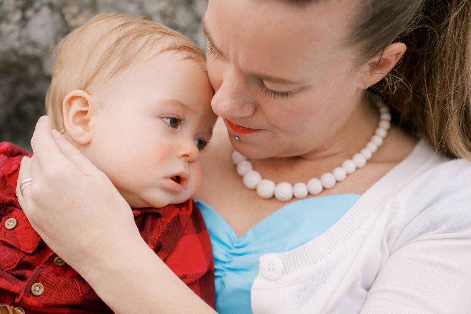 A mother tenderly holds her baby close, wearing a pearl necklace and blue dress, sharing an intimate moment.