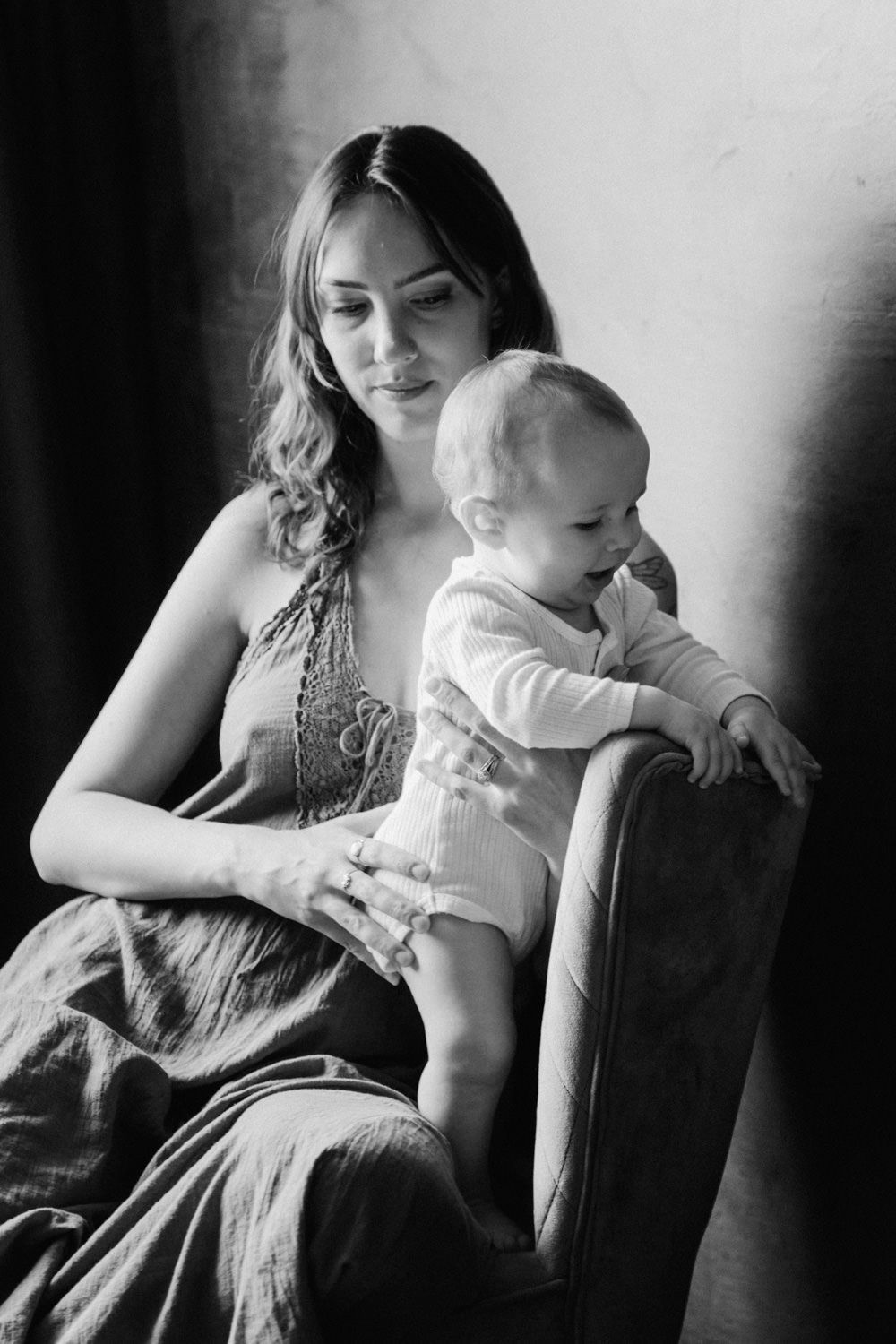 Black and white portrait of a young mother sitting in armchair tenderly holding her baby infant.