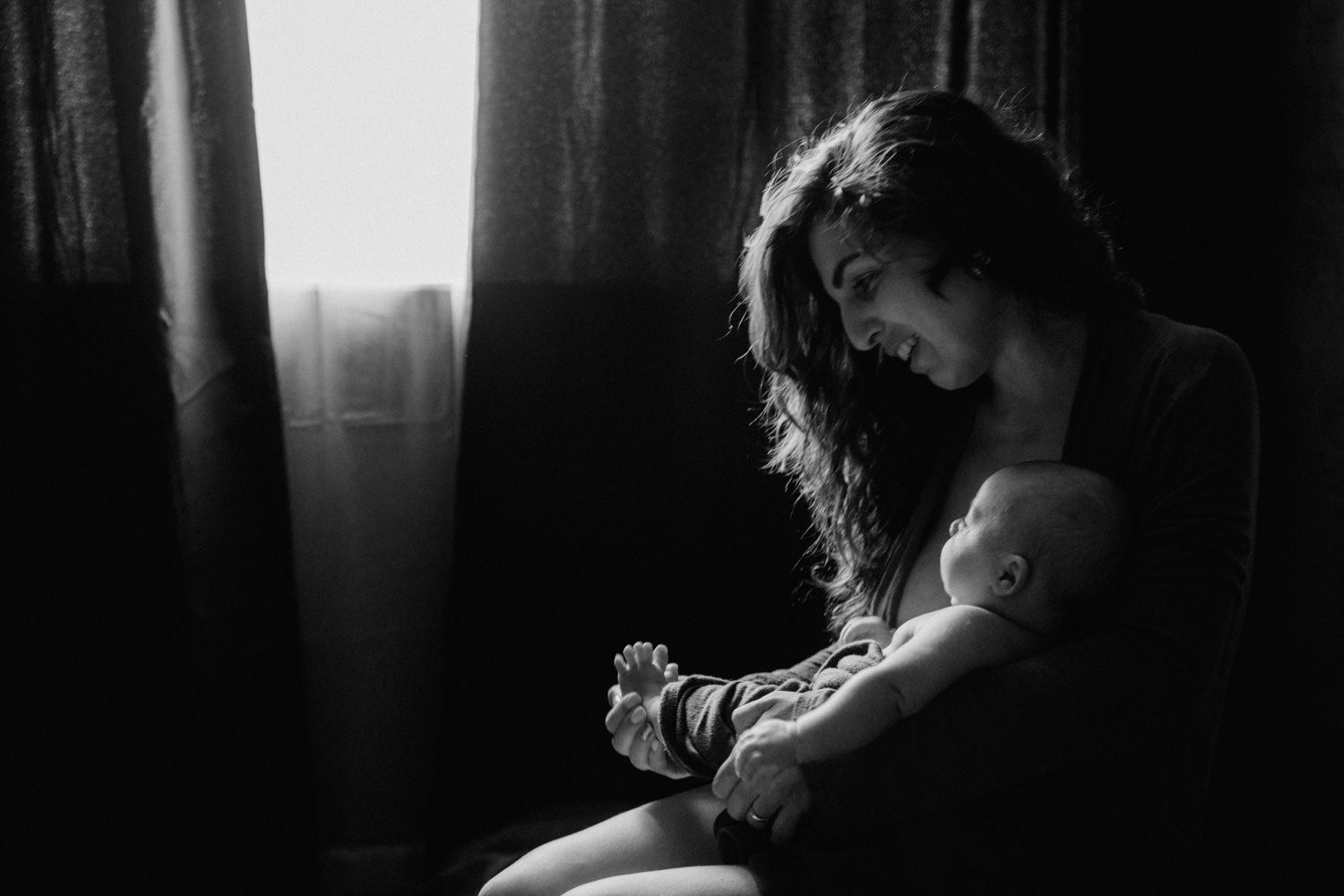 Black and white photo of a mother tenderly holding her newborn baby near a window.