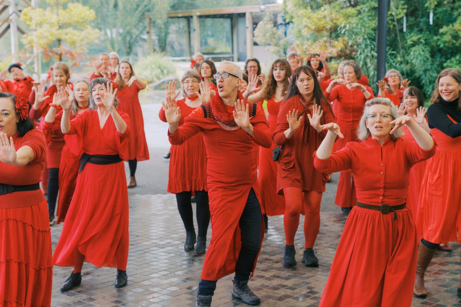Large group of women in red dresses performing a synchronized dance outdoors.