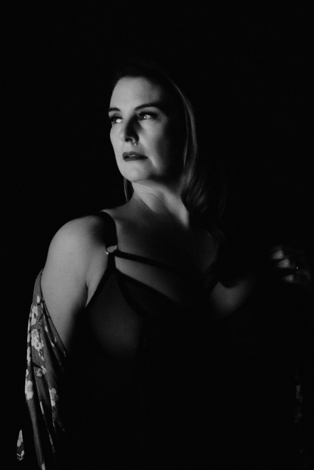 Black and white portrait of a woman in a dark studio, dramatic lighting highlighting her face and bare shoulder.