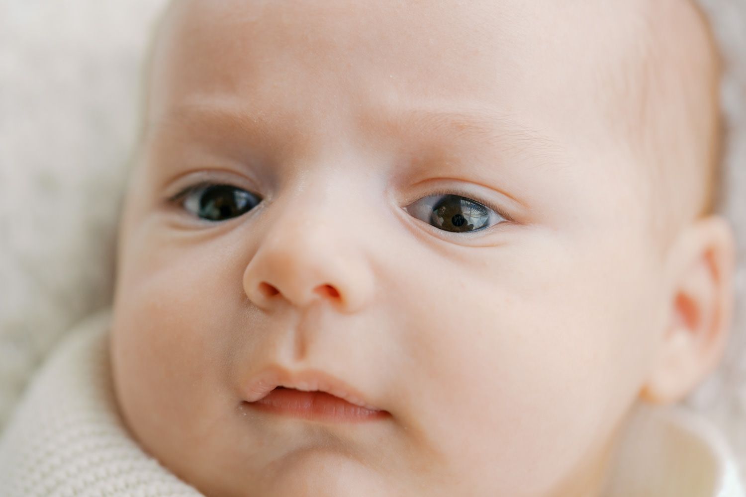 Close-up portrait of a newborn baby with big blue eyes and soft skin in a white outfit.
