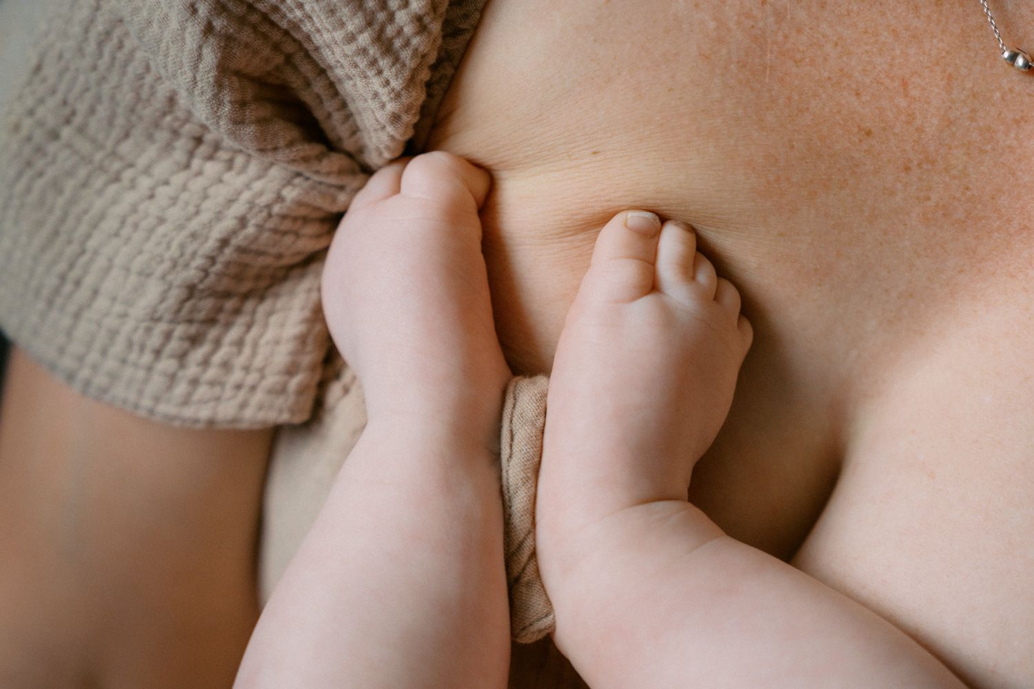 Close-up of a newborn baby's tiny feet resting against a mother's chest during breastfeeding.