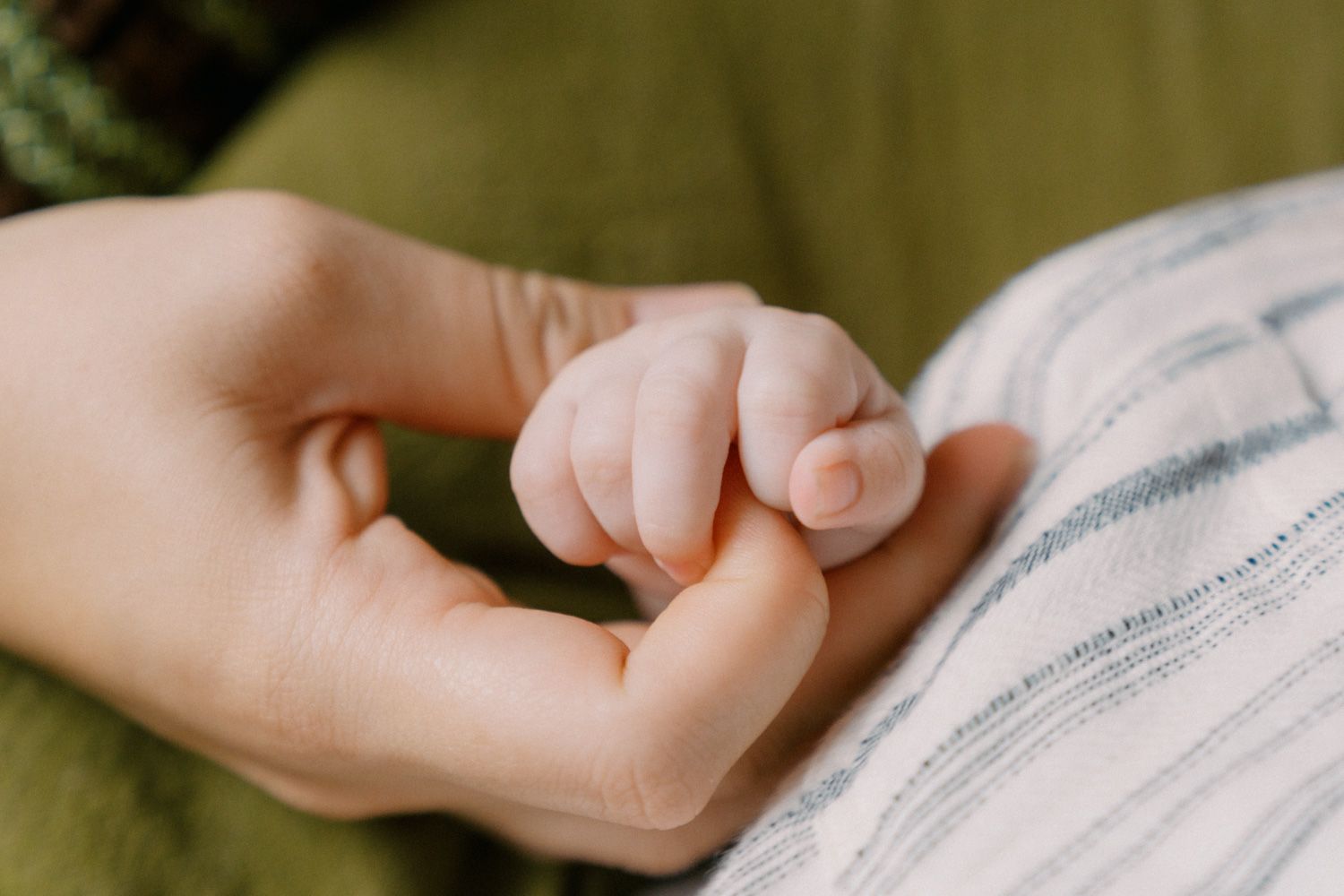 A newborn baby grasping an adult finger, symbolizing the tender bond between parent and child.