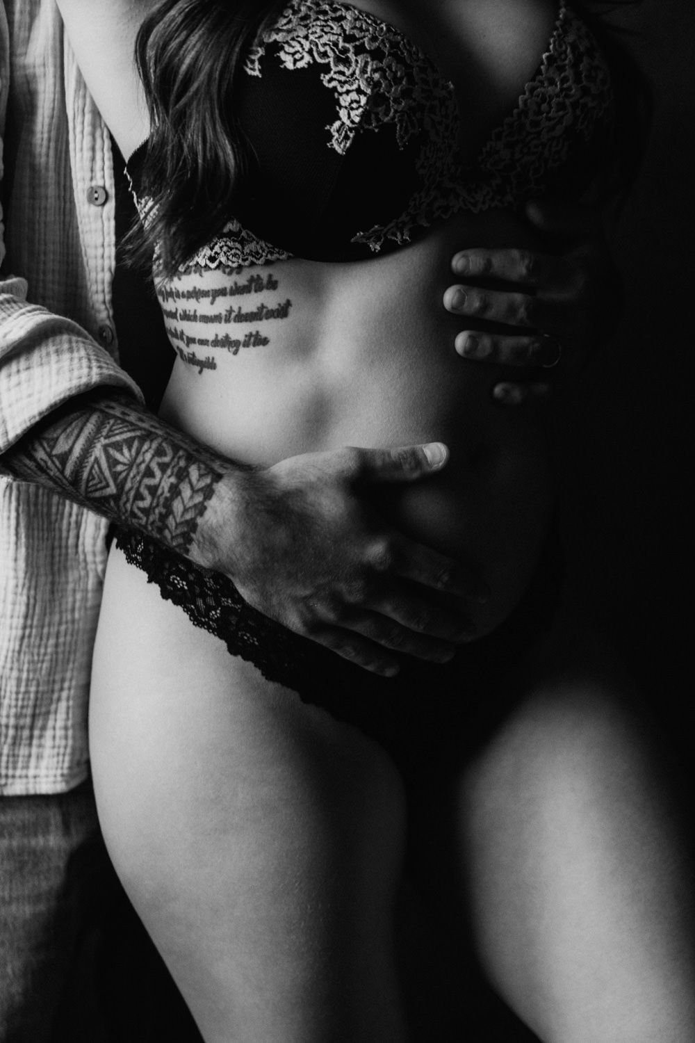 Black and white photo of a couple embracing, man with tribal tattoo holding woman in lace lingerie.
