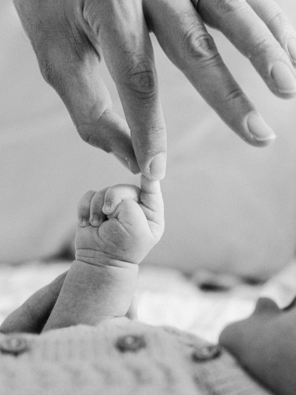 Black and white close-up of a newborn baby's tiny hand gripping a parent's finger.