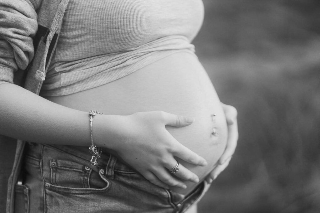 Black and white close-up of pregnant woman cradling baby bump wearing jeans and a bracelet.