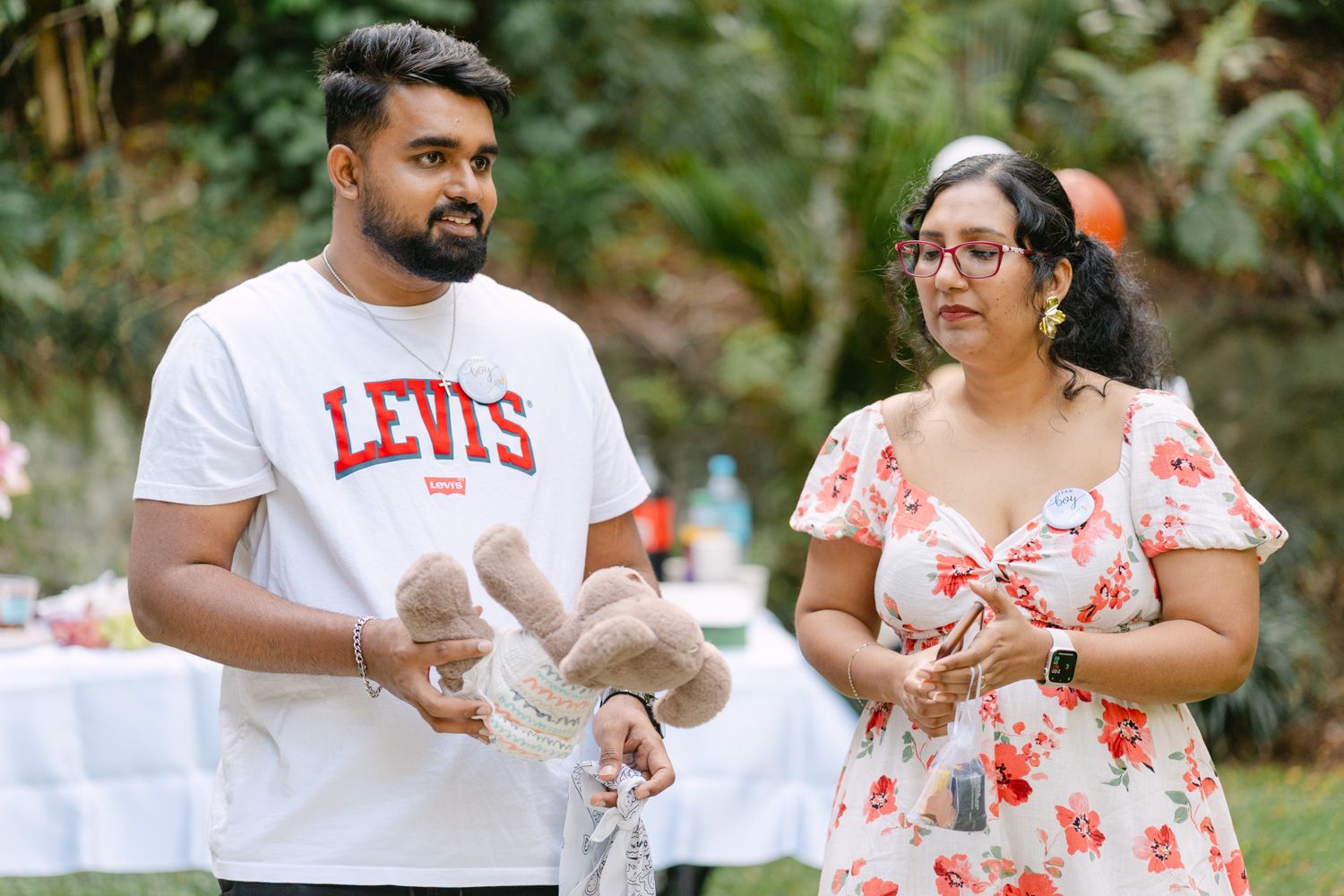 A man in a Levis shirt and a woman in a floral dress stand together at an outdoor celebration holding stuffed animals.